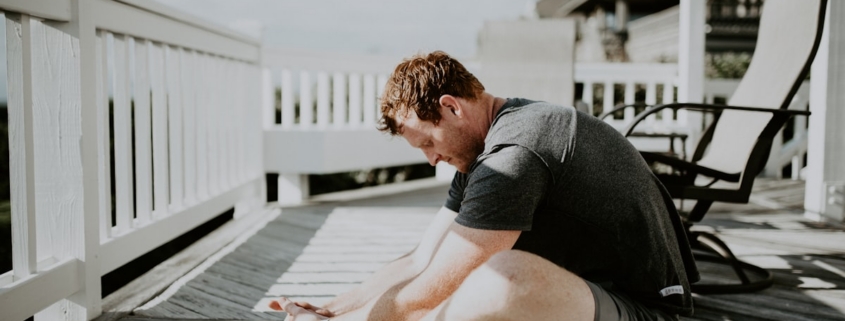 Adult doing a seated forward stretch on a sunlit deck, illustrating non-opioid approaches to chronic pain in residential care