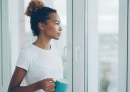 Adult sitting peacefully by a sunlit window with a warm mug, illustrating quiet, hopeful moments in recovery during a sober Memorial Day weekend.