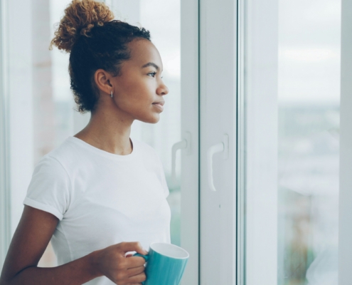Adult sitting peacefully by a sunlit window with a warm mug, illustrating quiet, hopeful moments in recovery during a sober Memorial Day weekend.