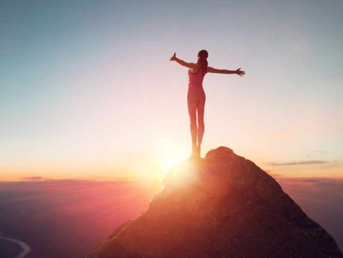 woman standing at the top of a mountain arms out wide at sunset